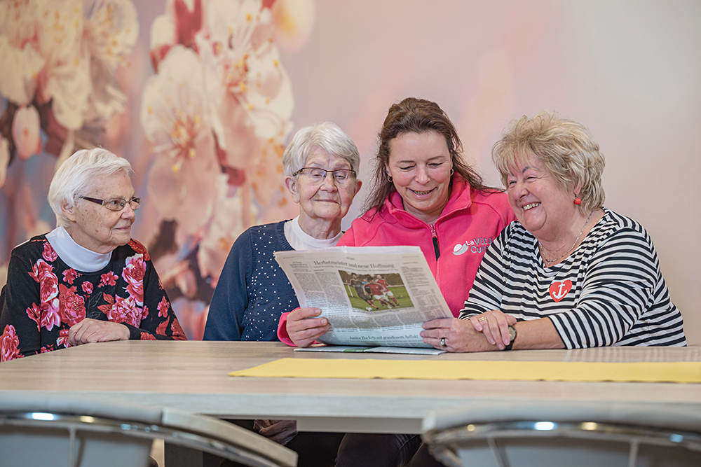 Mitarbeiterin der LaVitaCura Pflegedienst GmbH liest mit 3 Seniorinnen in der Tagespflege die Zeitung ©LaVitaCura Pflegedienst GmbH